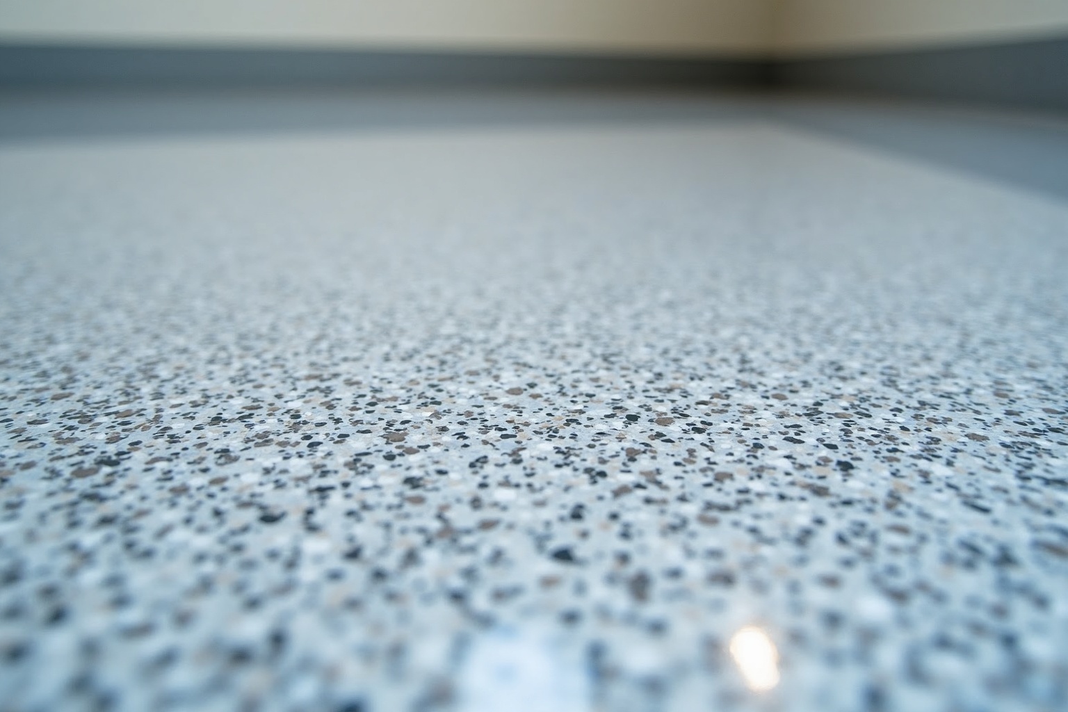 A technician spreads a thick layer of glossy resin across a prepared concrete garage floor. The wet surface creates mirror-like reflections of the overhead lighting while highlighting the smooth texture.