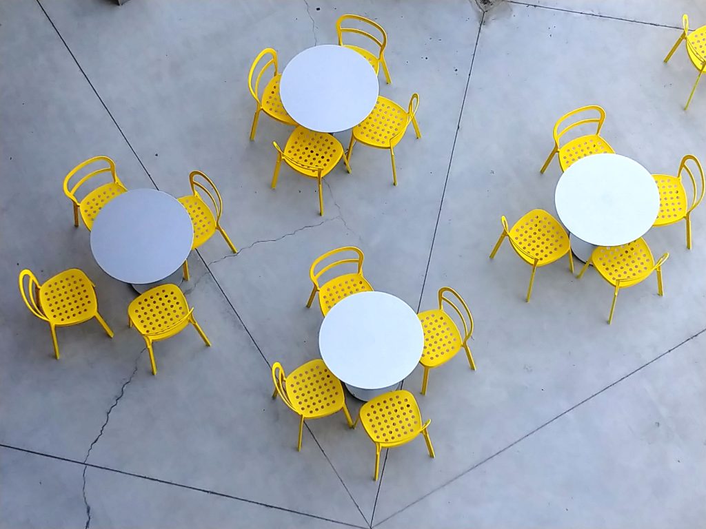 Aerial shot of outdoor seating with vibrant yellow chairs and white tables on concrete.