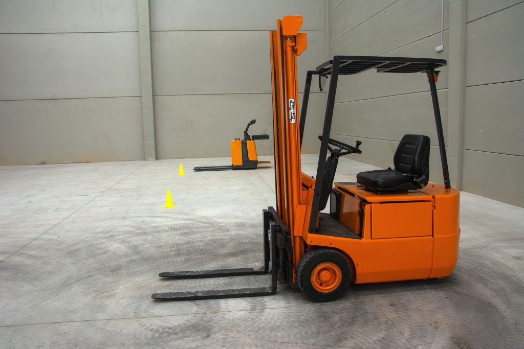 An orange forklift in a spacious warehouse with concrete floors and minimal equipment.