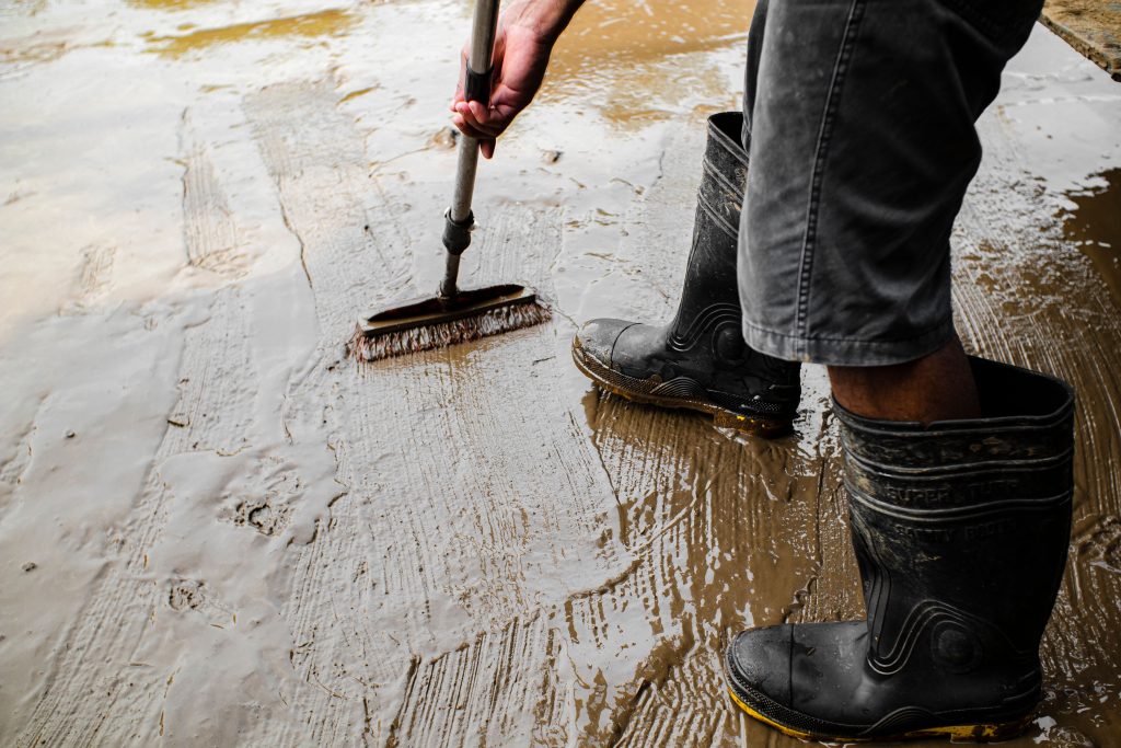 Male worker priming a cement floor with a brush in rubber boots